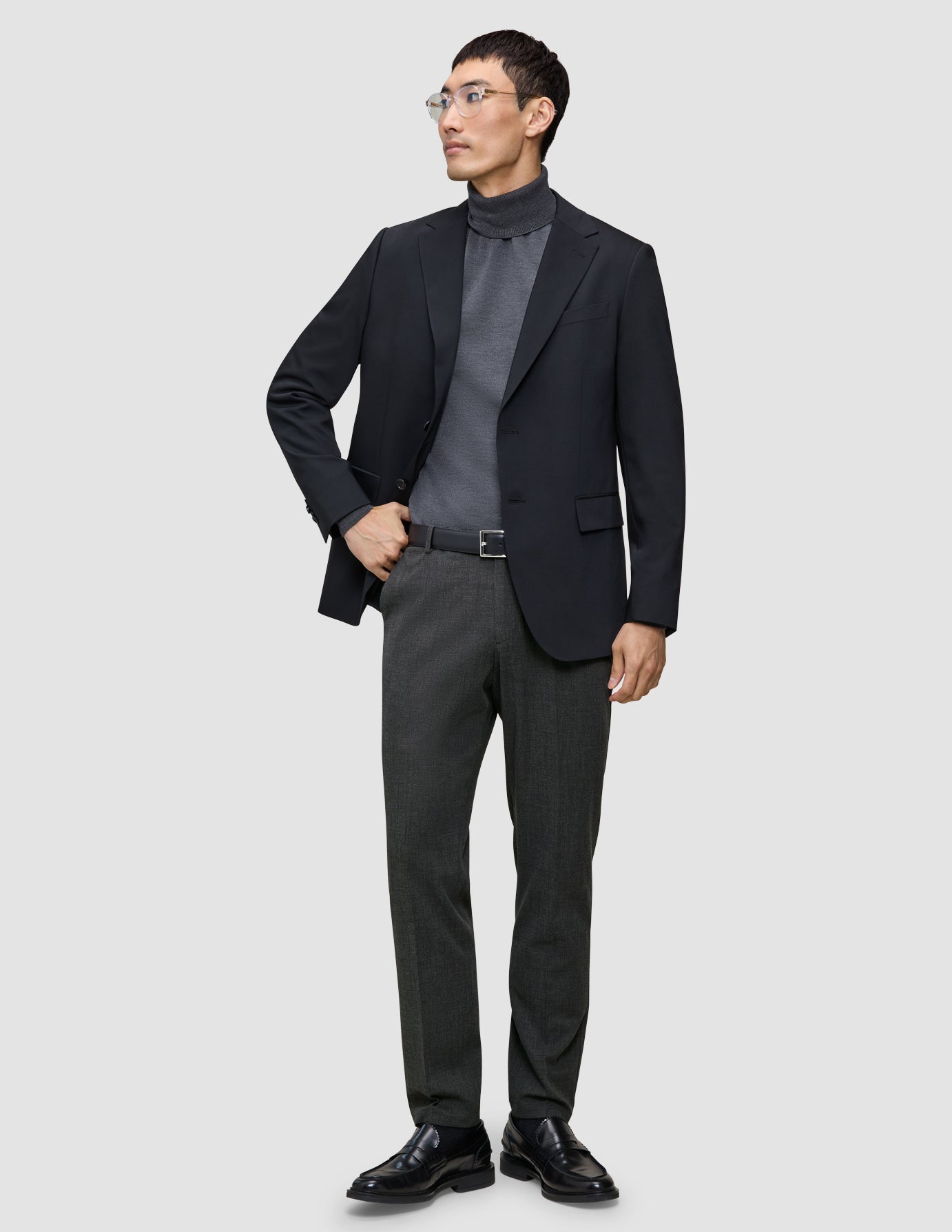 En mand i en sort blazer, en grå rullekravebluse og et par Motion Suit-bukser i farven Regular Pepper Grey.